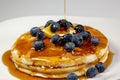 Pouring syrup over the butter on the blueberry stack of pancakes on the kitchen table waiting to be eaten Royalty Free Stock Photo