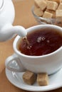 Pouring black tea into a cup with brown sugar on background