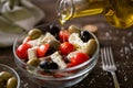 pouring virgin olive oil on vegetarian salad with fresh vegetables, feta and green olives. Royalty Free Stock Photo