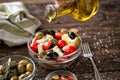 pouring virgin olive oil on vegetarian salad with fresh vegetables, feta and green olives. Royalty Free Stock Photo
