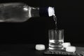 Pouring vodka from bottle in glass and ice cubes on black table Royalty Free Stock Photo