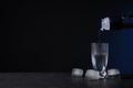 Pouring vodka from bottle into shot glass on black table against dark background. Space for text Royalty Free Stock Photo