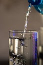 Pouring water from blue plastic bottle into a glass on blurred background. Selective focus, shallow DOF and copy space Royalty Free Stock Photo