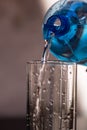 Pouring water from blue plastic bottle into a glass on blurred background. Selective focus, shallow DOF and copy space Royalty Free Stock Photo