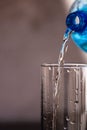 Pouring water from blue plastic bottle into a glass on blurred background. Selective focus, shallow DOF and copy space Royalty Free Stock Photo