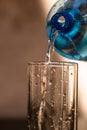 Pouring water from blue plastic bottle into a glass on blurred background. Selective focus, shallow DOF and copy space Royalty Free Stock Photo