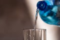 Pouring water from blue plastic bottle into a glass on blurred background. Selective focus, shallow DOF and copy space Royalty Free Stock Photo