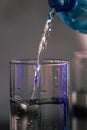 Pouring water from blue plastic bottle into a glass on blurred background. Selective focus, shallow DOF and copy space Royalty Free Stock Photo