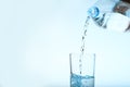 Pouring water from bottle into glass against blue background Royalty Free Stock Photo