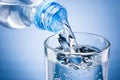 Pouring water from bottle into glass on blue background Royalty Free Stock Photo