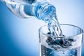 Pouring water from bottle into glass on blue background Royalty Free Stock Photo