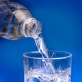 Pouring water from bottle into glass on blue background Royalty Free Stock Photo