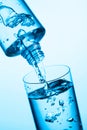 Pouring water from a bottle into glass on a blue background Royalty Free Stock Photo