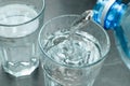 Pouring water from bottle into glass on grey background. Refreshing drink. Healthy lifestyle and stay hydrated