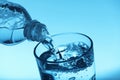 Pouring water from bottle into glass on light blue background, closeup Royalty Free Stock Photo