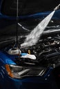 Pouring water on car engine. Washing car engine with spray, brush and detergent in detailing auto service. Detailing Royalty Free Stock Photo