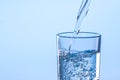 Pouring water into glass against light blue background, closeup. Space for text Royalty Free Stock Photo