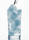 Pouring water in a glass full of ice cubes, white background, blue toned object Royalty Free Stock Photo