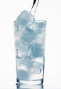 Pouring water in a glass full of ice cubes, white background, blue toned object Royalty Free Stock Photo