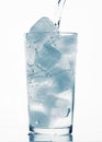 Pouring water in a glass full of ice cubes, white background, blue toned object Royalty Free Stock Photo