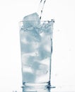 Pouring water in a glass full of ice cubes, white background, blue toned object Royalty Free Stock Photo