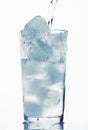 Pouring water in a glass full of ice cubes, white background, blue toned object Royalty Free Stock Photo