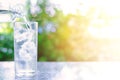 Pouring water into a glass of ice on blurred natural green background