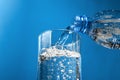 Pouring water from plastic bottle into glass on blue background. Stream of clean water flowing in a glass Royalty Free Stock Photo