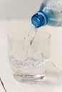 Pouring water from a plastic bottle into a glass. White wood background. Royalty Free Stock Photo