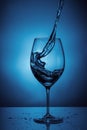 Pouring water into a transparent glass for wine. blue background with water splashes Royalty Free Stock Photo