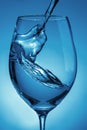 Pouring water into a transparent glass for wine close-up. light blue background with water splashes Royalty Free Stock Photo