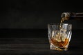 Pouring whiskey from bottle into glass with ice cubes on table Royalty Free Stock Photo