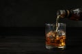 Pouring whiskey from bottle into glass with ice cubes on table. Royalty Free Stock Photo