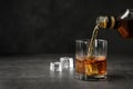 Pouring whiskey from bottle into glass with ice cubes on table. Royalty Free Stock Photo