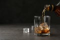 Pouring whiskey from bottle into glass with ice cubes on table. Royalty Free Stock Photo