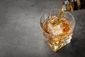 Pouring whiskey from bottle into glass with ice cubes on table Royalty Free Stock Photo