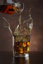 Pouring whiskey from bottle in to glass with ice cubes  on table Royalty Free Stock Photo