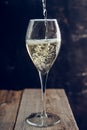 Pouring white wine in glass on the rustic wooden background