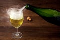 Pouring wine or champagne from the green bottle into the wine glass with some smoke on wooden background, for celebration or party Royalty Free Stock Photo