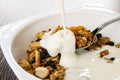 Pouring yogurt in bowl with cereal breakfast with peanut, raisin on wooden table