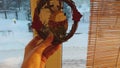 POV hanging Christmas wreathe with funny hedgehog on window pane. Decorating home in winter. Eco style Christmas decor