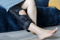 POV injured woman in knee immobilizer resting on living room at home, leg closeup