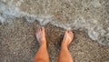 POV of male feet standing on the sea beach and enjoying rolling calm waves with clear water. Holiday, summer vacation Royalty Free Stock Photo