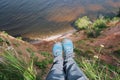 POV person feet in sneackers hanging from high send coast over lake or sea. Top view woman legs dangling over water. Personal Royalty Free Stock Photo