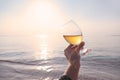 Pov photo of woman hand holding glass of white wine over sea sunset on the beach Royalty Free Stock Photo