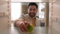 POV point of view from inside refrigerator Caucasian adult happy man at kitchen open empty fridge take last green apple Royalty Free Stock Photo