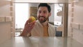 POV point of view from inside refrigerator Caucasian adult happy man at kitchen open empty fridge take last green apple Royalty Free Stock Photo