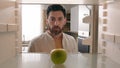POV point of view from inside refrigerator Caucasian adult man at kitchen open empty fridge with one green apple fruit Royalty Free Stock Photo