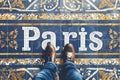 a pov shot looking down on a persons feet standing on a mosaic tiled floor with the word Paris