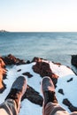 POV view of legs and shoes on background of snow rock and ocean. Brave explorer sits in front of snowy cliff and look on feet. Adv